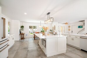 A modern kitchen with white cabinetry, a central island, and a dining area with a view. - St Pete Beach Waterfront Pool Hot Tub (St Pete Beach)
