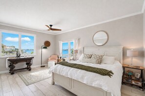 Une chambre à coucher comprenant un lit, un ventilateur de plafond, une fenêtre avec vue, une table de chevet et une commode.