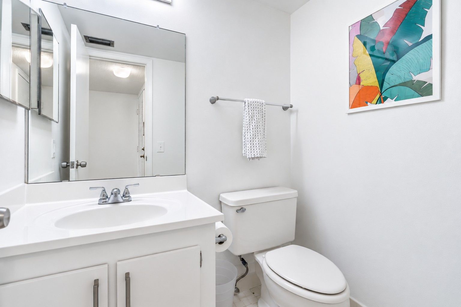 A bathroom with a white sink, mirror, toilet, and a towel rack.