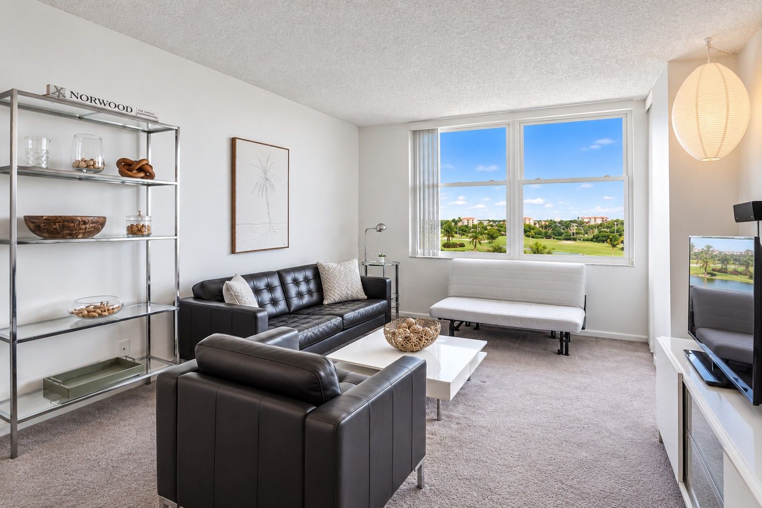 A modern living room with a black leather sofa, a white bench, and a glass shelving unit with decorative items.