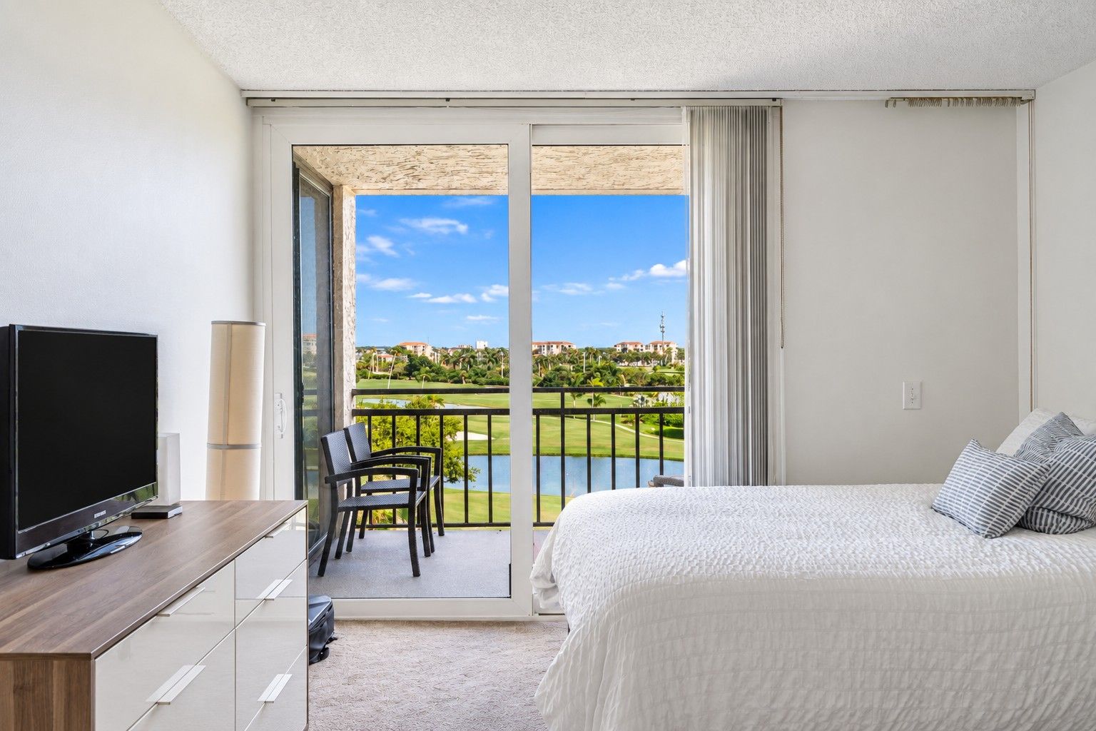 Quarto de hotel com cama, televisão, escrivaninha e varanda com vista para um campo de golfe.