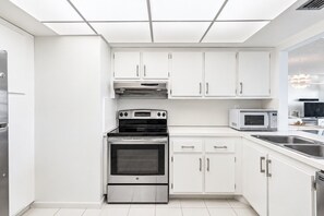 Eine moderne Küche mit weißen Schränken, einem Backofen, einer Mikrowelle und einem Edelstahl-Kühlschrank.