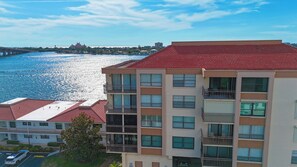 A multi-story building with balconies, a parking area, and a view of a river with a bridge in the background. - Bayway Isles Isla Del Sol Bahia Del Mar Pool (St Petersburg)