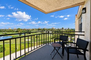 Ein Balkon mit Blick auf einen Golfplatz, ein kleiner Tisch und zwei Stühle.