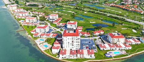 Un complejo turístico frente al mar con varias edificaciones, un campo de golf y un puerto deportivo.