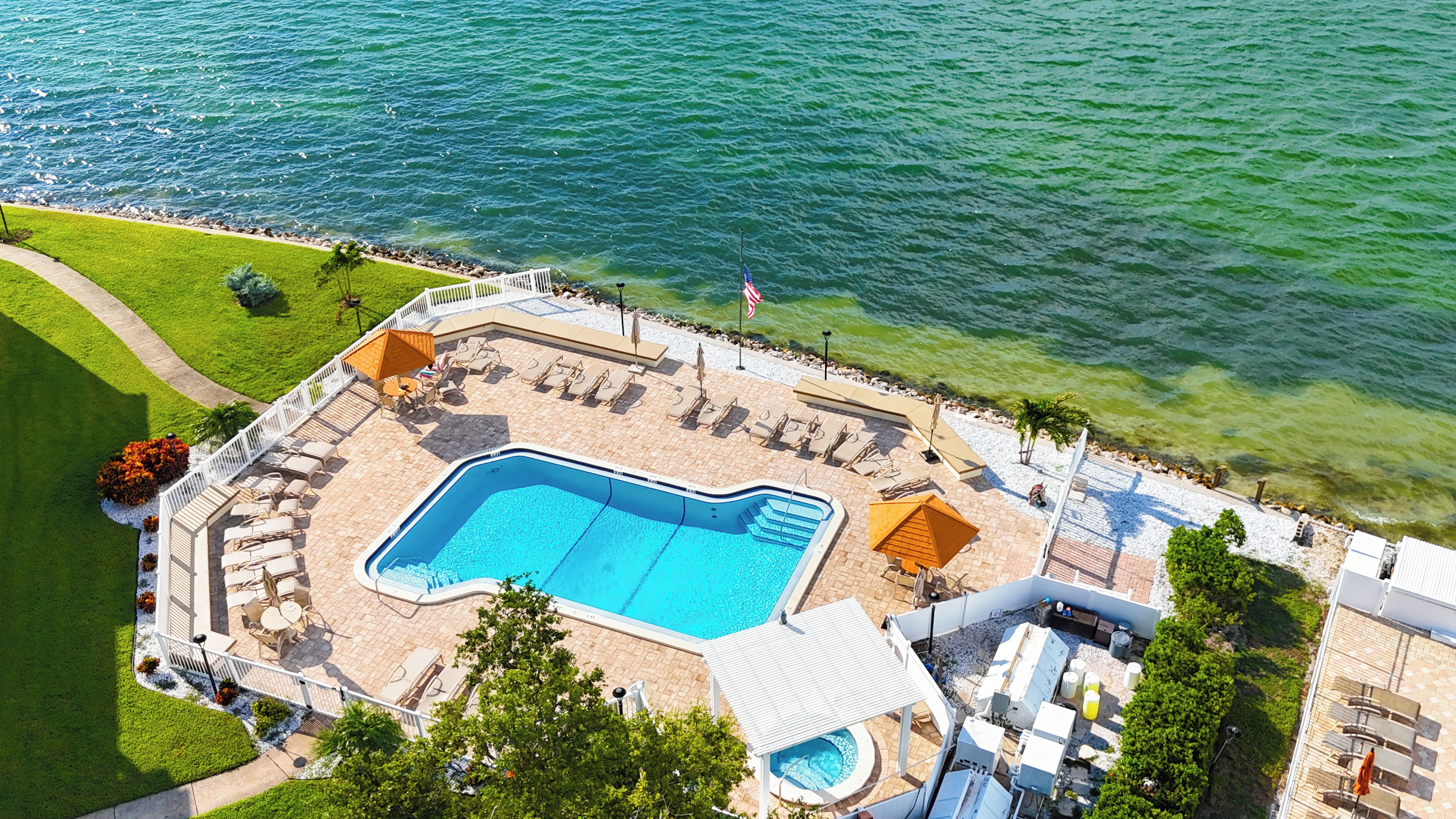 Luftaufnahme eines Resorts mit Swimmingpool, Liegestühlen und einer Flagge.