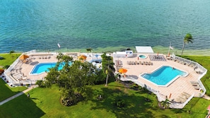 A resort with two swimming pools, sun loungers, umbrellas, and a view of the sea. - Bayway Isles Isla Del Sol Bahia Del Mar Pool (St Petersburg)
