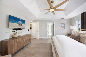 Ein Schlafzimmer mit einem großen Bett, einem Deckenventilator, einem Fernseher und einer Tür zu einem anderen Raum.