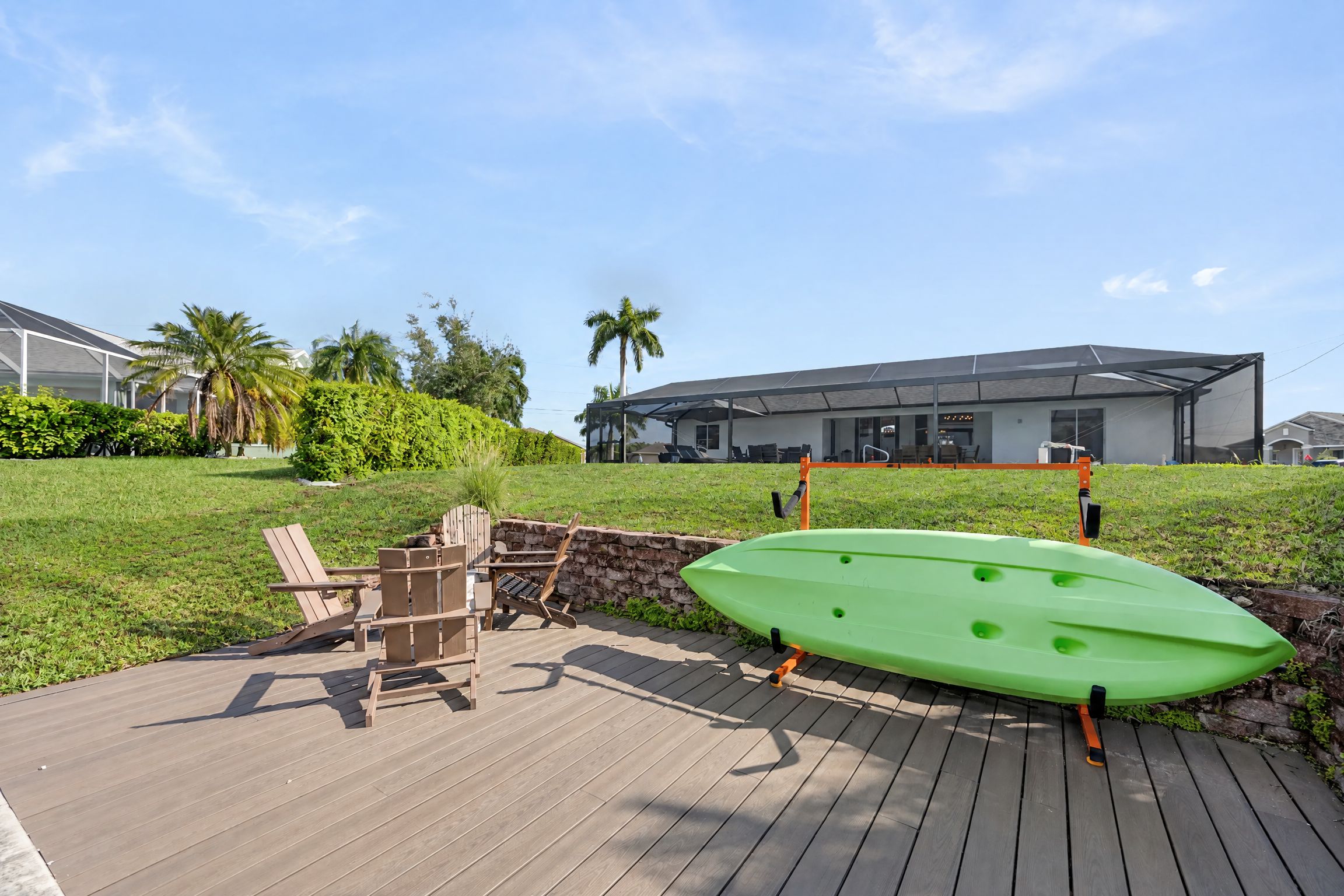 Een houten terras met een groene kajak, een houten stoel en een stenen muur.