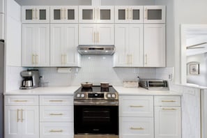 A modern kitchen with white cabinets, gold handles, a built-in oven, a coffee maker, and a toaster. - New Luxury 4BR Gulf-Access Canal Villa with Heated Pool, AC, & Central Location (Cape Coral)