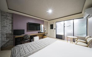 Ein modernes Hotelzimmer mit einem großen Bett, einem Schreibtisch mit Computer, einem Fernseher und einer Sitzecke mit Stühlen.