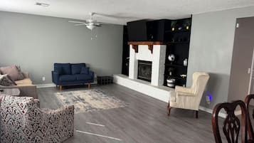 A living room with a blue sofa, patterned ottoman, and a fireplace.