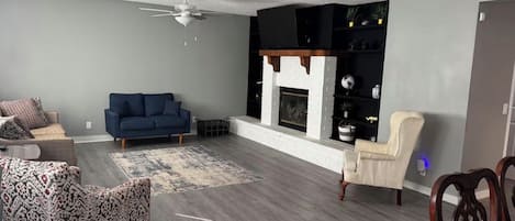A living room with a blue sofa, patterned ottoman, and a fireplace.