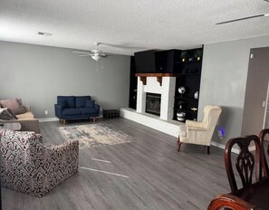A living room with a blue sofa, patterned ottoman, and a fireplace.