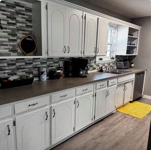 A kitchen with white cabinets, a tiled backsplash, and a yellow rug.