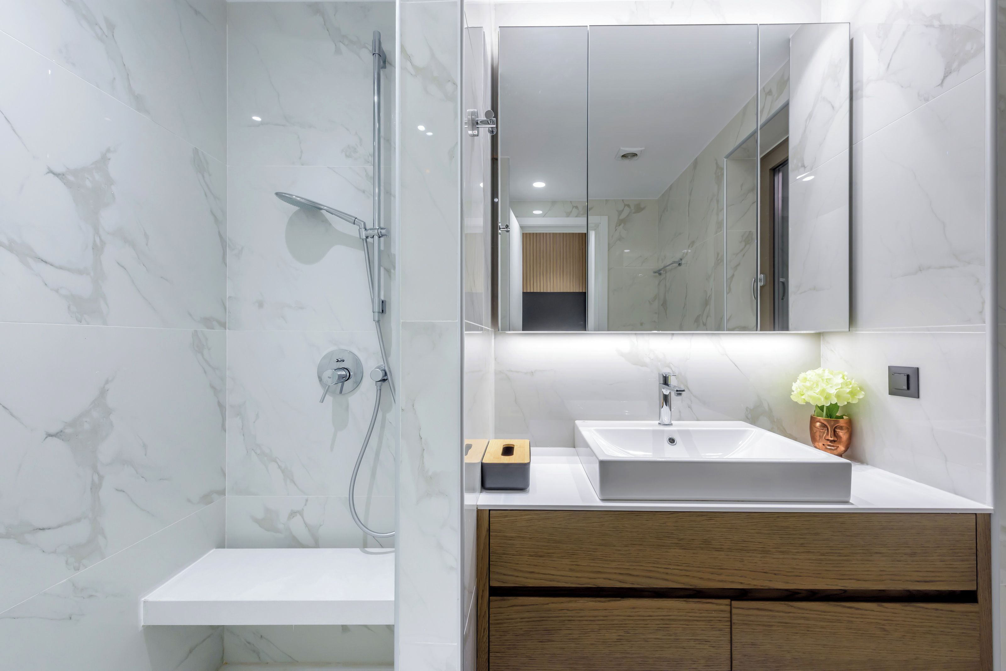 A modern bathroom with a marble shower, a wooden vanity, and a white sink.