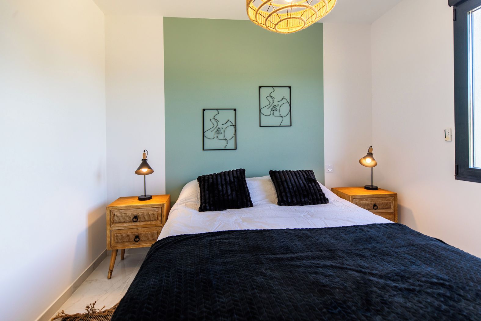 A bedroom with a bed, two bedside tables with lamps, a window, and two wall art pieces.