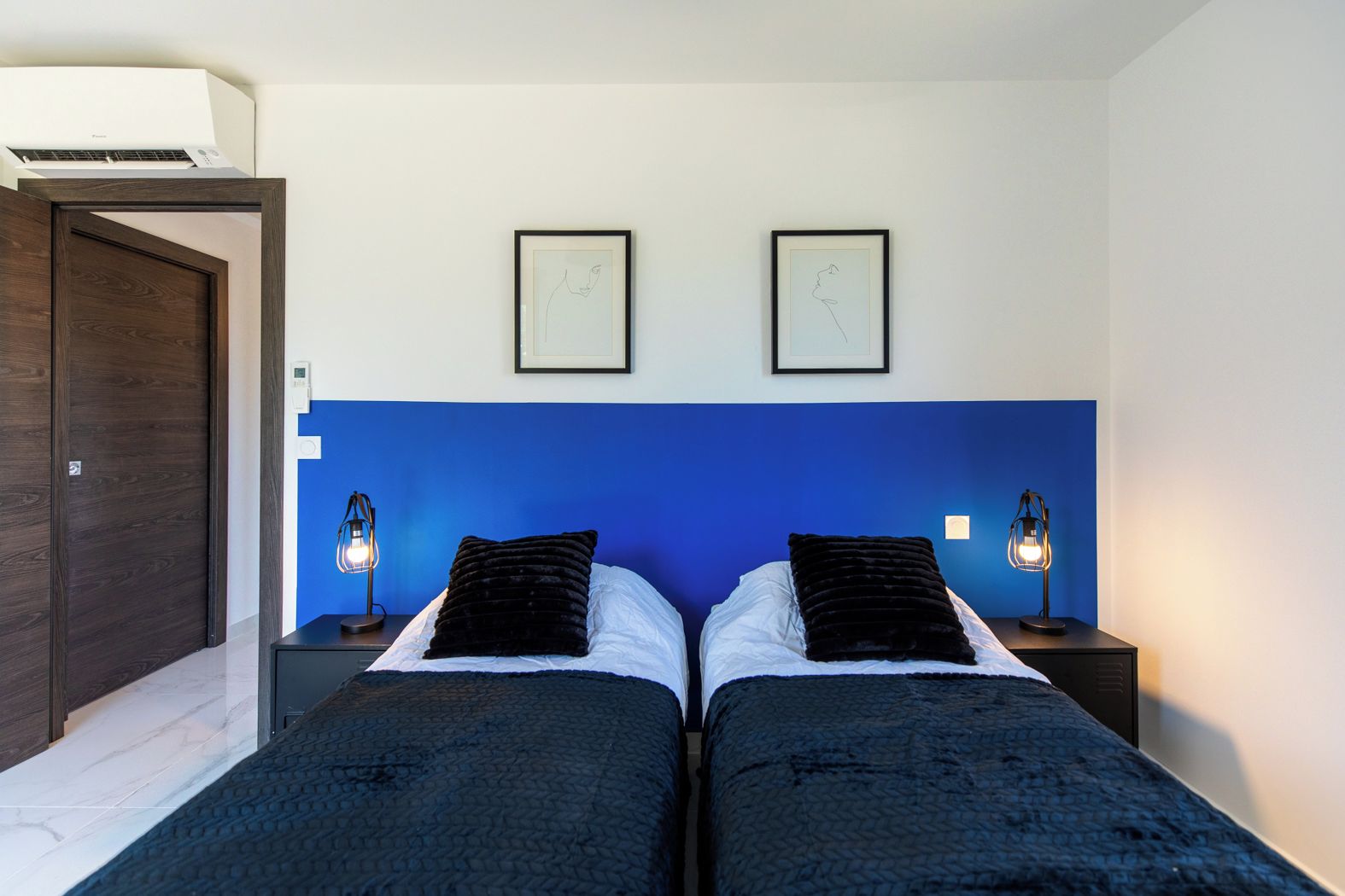 A hotel room with two beds, a blue accent wall, framed artwork above the beds, and bedside lamps.