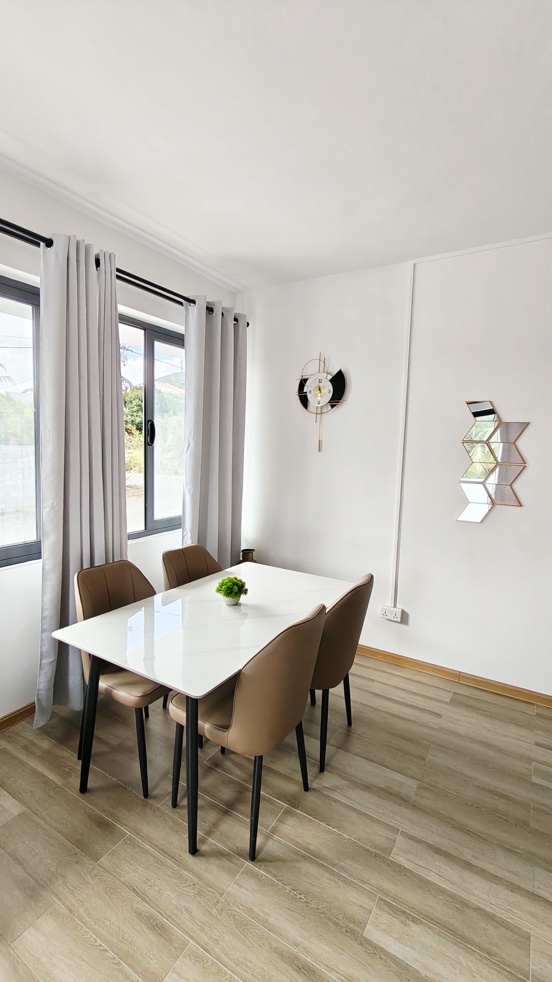 A dining area with a white table, four chairs, a clock, and a geometric wall decoration.