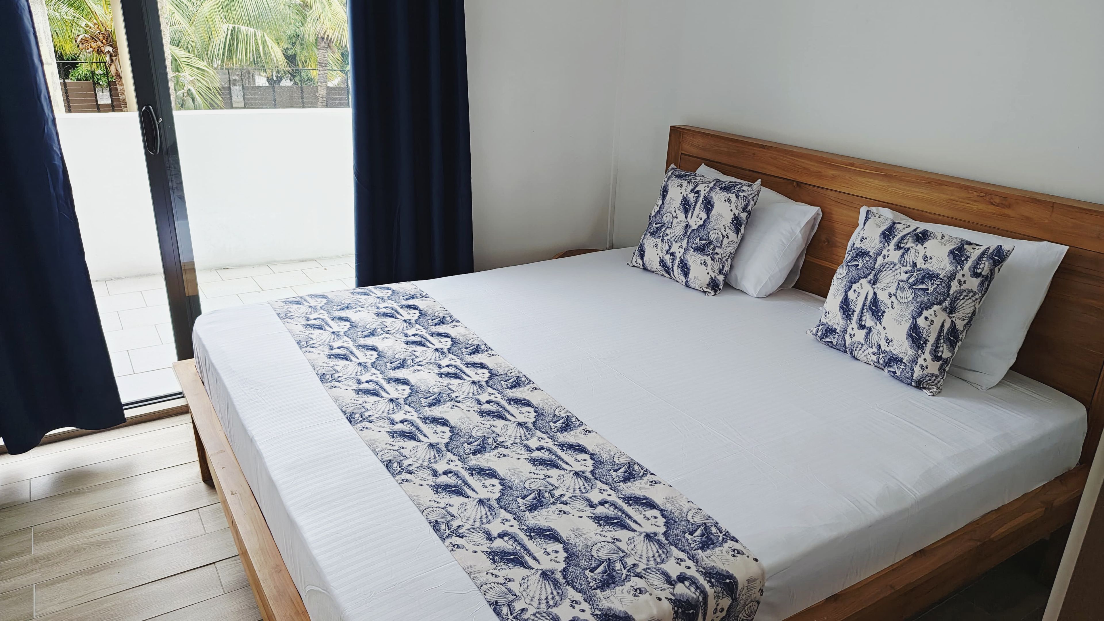A bed with a wooden headboard, white bedding, and blue patterned pillows.