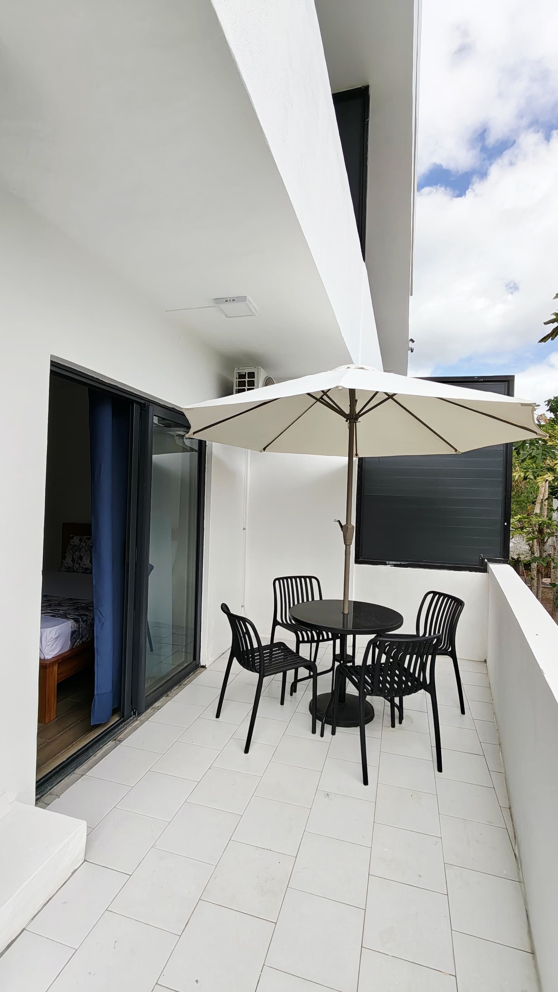 A balcony with a table and chairs, a sliding glass door, and a white tiled floor.
