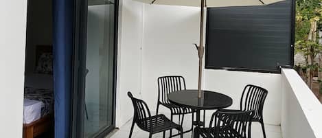 A balcony with a table and chairs, a sliding glass door, and a white tiled floor.