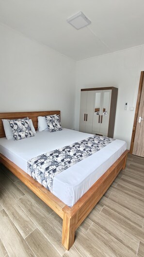 A bedroom with a wooden bed, white bedding, a wardrobe, and a door.