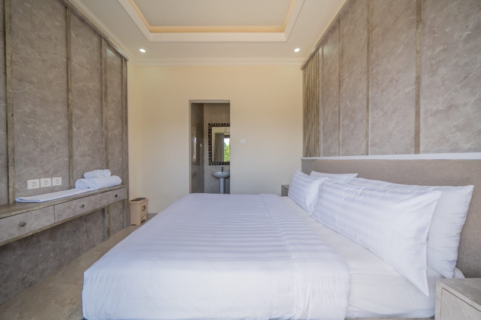 A hotel room with a large bed, a bedside table, a mirror, and a view of the bathroom.