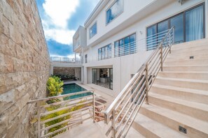 A modern building with a pool, outdoor staircase, and a stone wall. - Gorgeous 8-bedroom house with great facilities. (Bali)