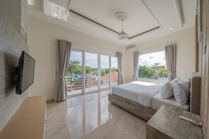 A modern bedroom with a large bed, a flat-screen TV, and a balcony with a view of buildings and trees.