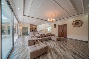 A spacious living area with a large sectional sofa, a chandelier, and a clock on the wall. - Gorgeous 8-bedroom house with great facilities. (Bali)