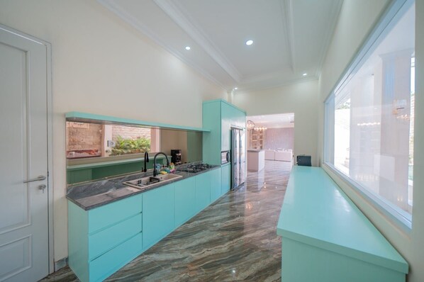 A modern kitchen with teal cabinetry, a marble countertop, and a view to the living area.