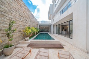 A modern outdoor pool area with stone walls, lounge chairs, and a clear sky.