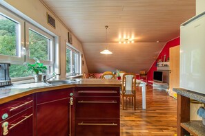 Une cuisine avec des meubles en bois, une table à manger, des chaises et une vue sur la verdure à l’extérieur.