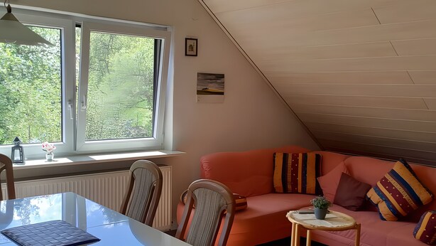 Ein gemütliches Zimmer mit schrägen Wänden, einem rosafarbenen Sofa, einem kleinen Tisch und einem Stuhl.