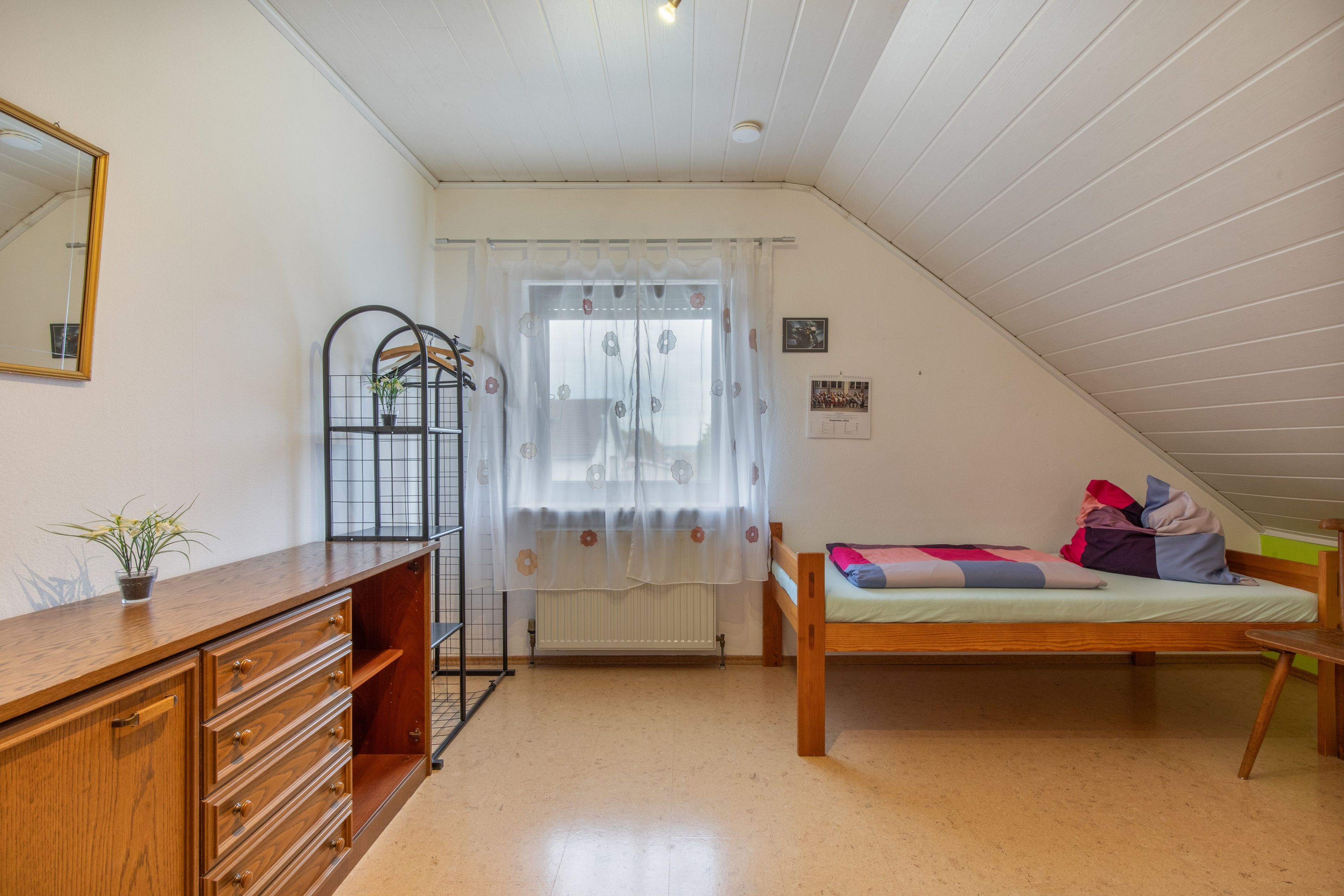 A bedroom with a wooden bed, a dresser, a mirror, and a window with curtains.