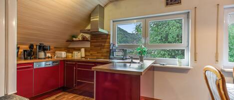 Una cocina moderna con suelo de madera, armarios rojos y un ventanal con vistas a zonas verdes.