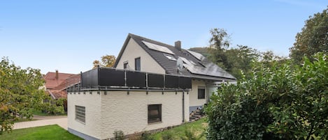 Una casa de un piso con techo inclinado, paneles solares y un pequeño jardín.