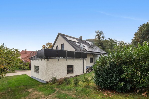 A single-story house with a sloped roof, solar panels, and a small garden area.