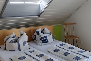 A room with a sloped ceiling, two beds with patterned bedding, a wooden chair, and a green wall. - Apartment in Green Setting by Rosenstein with Mountain View, Private Terrace, and Wi-Fi (Heubach)