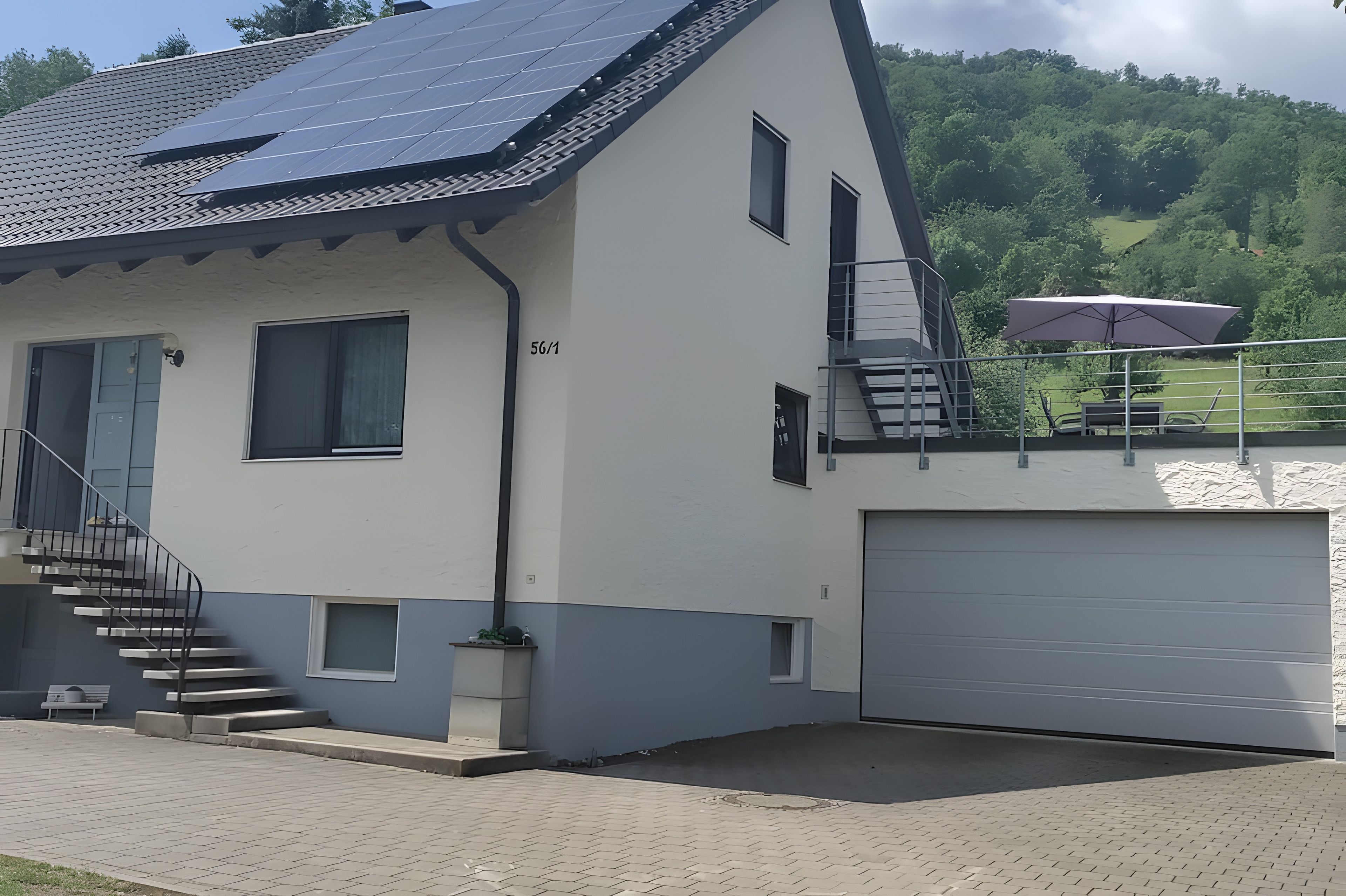 Uma casa moderna de dois andares, com garagem, escada e varanda com mesa e guarda-sol.