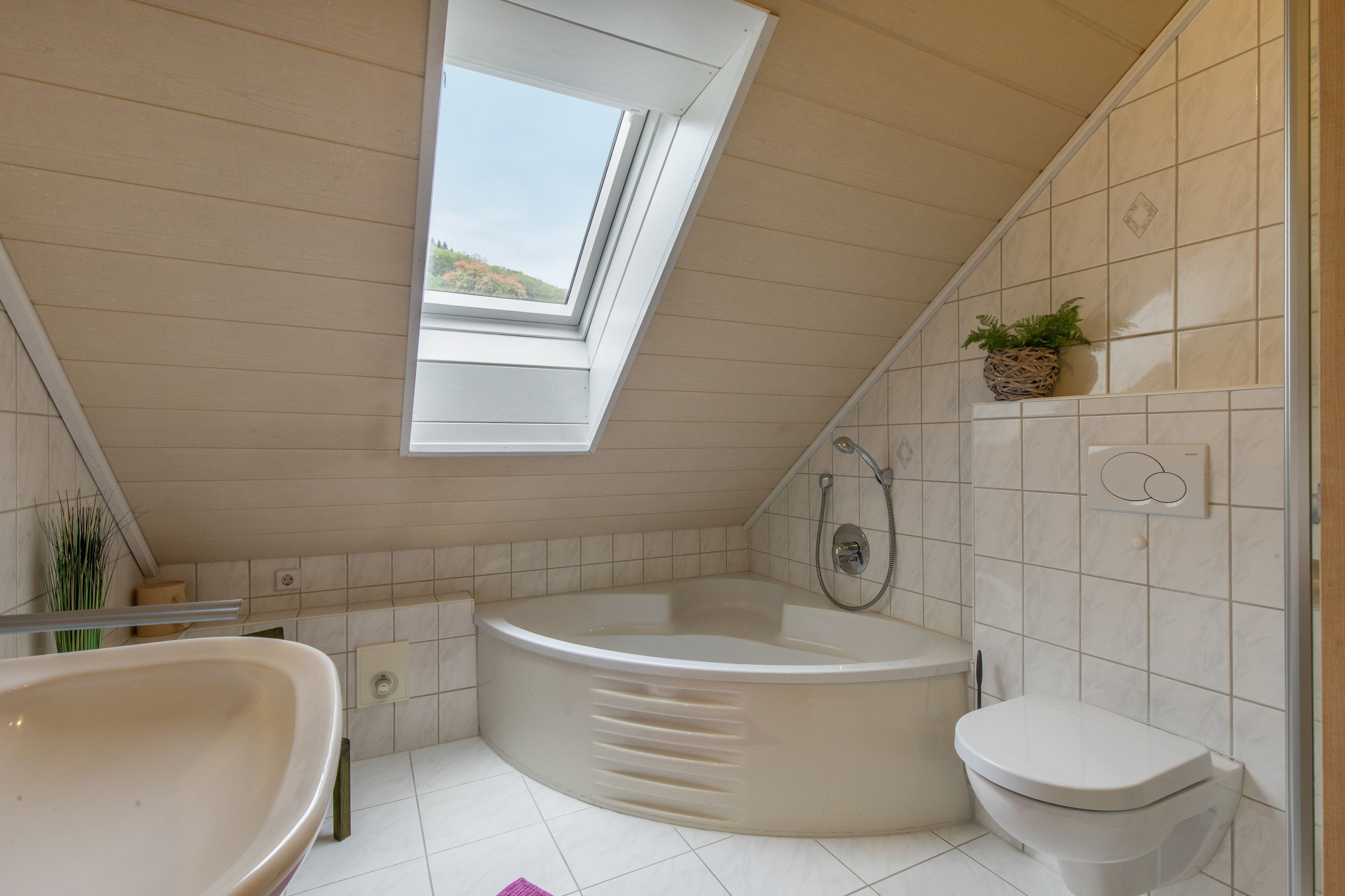 Et badeværelse med ovenlys, badekar, toilet og brusebad.