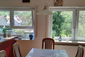 A room with a dining table, chairs, a radiator, and windows with views of greenery and buildings. - Apartment in Green Setting by Rosenstein with Mountain View, Private Terrace, and Wi-Fi (Heubach)