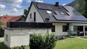 Ein modernes Haus mit Satteldach, Solaranlage und einer Glastür, die auf eine Terrasse führt.