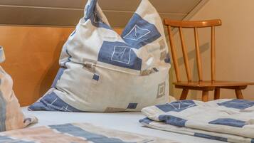 A bed with a blue and white patterned bedspread and pillows, a wooden chair, and a wall with a horizontal panel design.