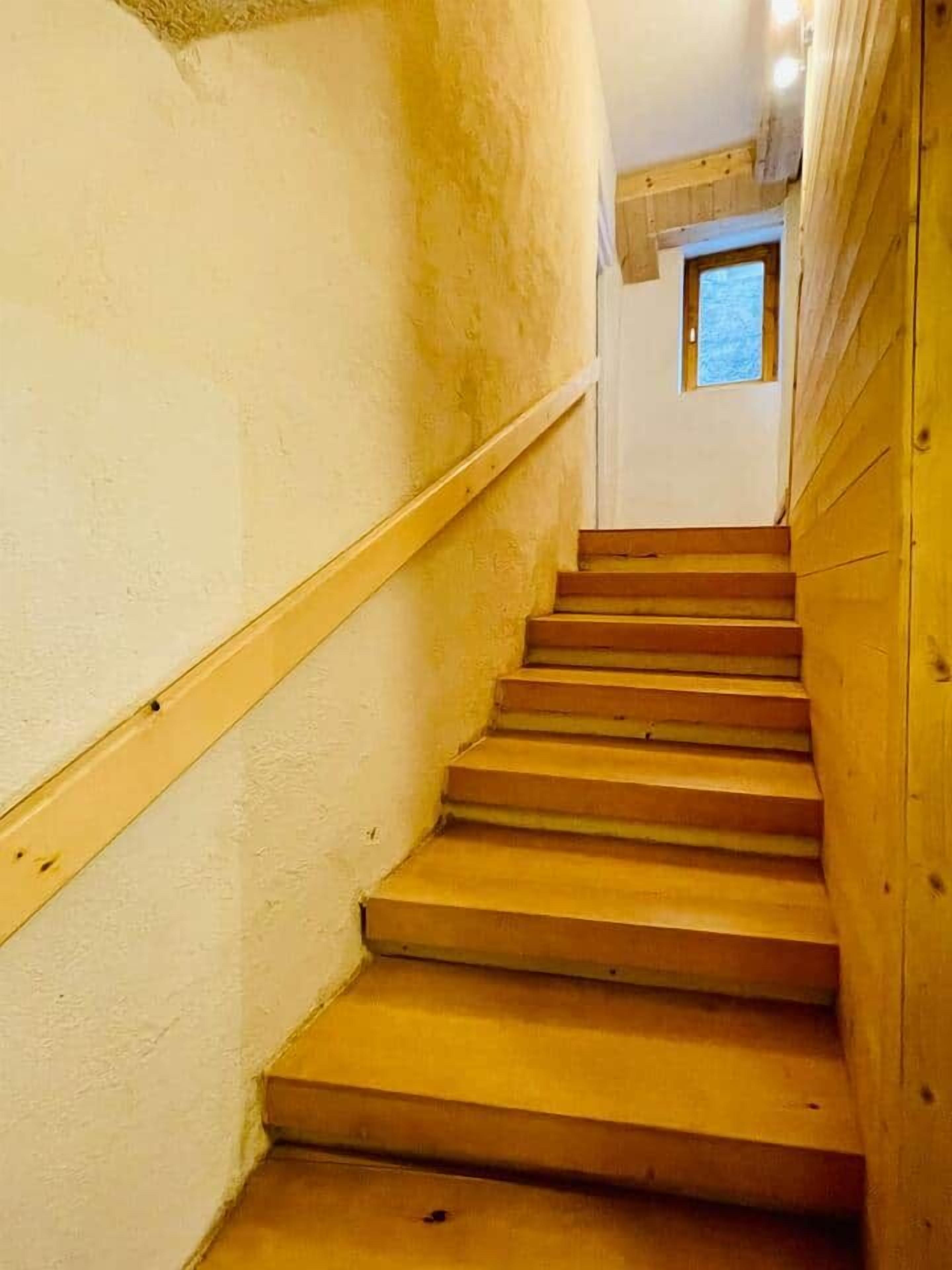 Un escalier en bois, doté d’une rampe, mène à un palier où se trouve une petite fenêtre.