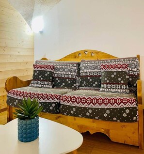 A wooden sofa with patterned cushions, a small table with a plant, and a wooden wall. - At Toutoune - Mountain Retreat - Sleeps 6, Aussois (Aussois)