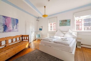 Quarto com cama, um banquinho, uma cadeira e obras de arte nas paredes.