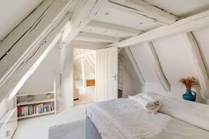 A bedroom with a sloped ceiling, a bed with white bedding, a bookshelf, and a vase with dried plants. - Stilhaus 1730 (Königsbach-Stein)