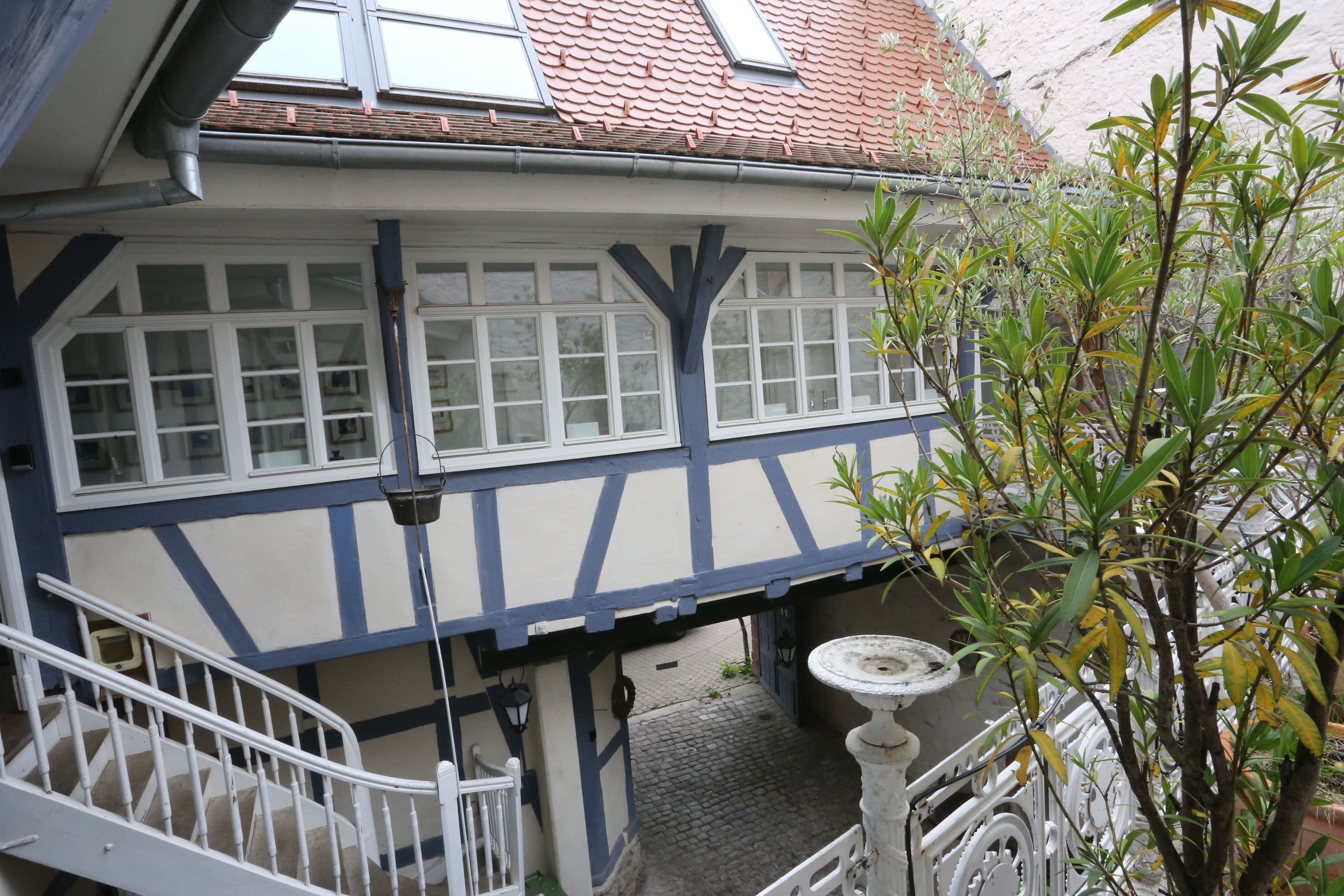 Un edificio tradicional con entramado de madera, con una escalera visible y un pequeño espacio exterior con un bebedero para pájaros.